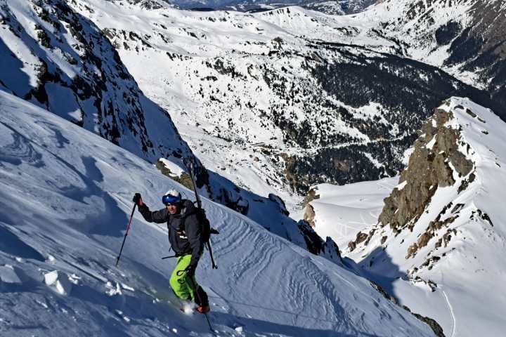 Skier in green pants descends a steep, snowy mountain slope on a sunny day.
