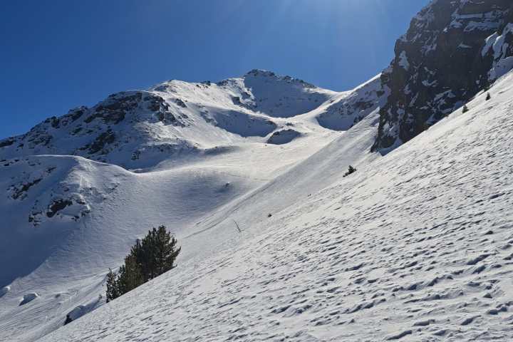 Snowy mountain slope under clear blue sky with bright sun shining.