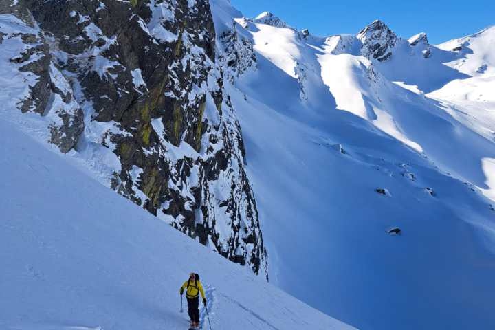 Skiers ascend a snowy mountainside under a clear blue sky.