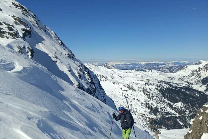 Person hiking up a snowy mountain slope under a clear blue sky.