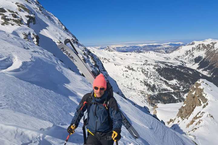 Person in bright pink hat skiing uphill on snowy mountain slope under clear blue sky.