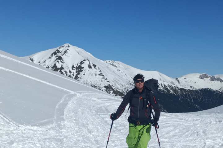 Person in green pants skiing on a snowy mountain slope under a clear blue sky.
