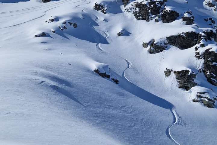 Snow-covered mountain peak with winding ski tracks under a clear blue sky.
