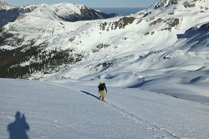 Person hiking on a snowy mountain slope under a clear blue sky.
