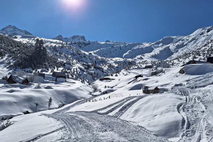 Snowy mountain landscape with cabins under a clear blue sky and bright sun.