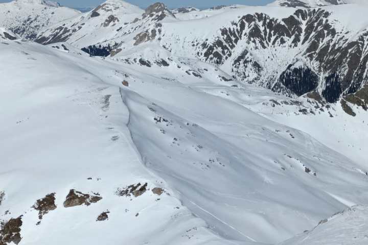 Person skiing on snowy mountain with clear blue sky and mountains in background.