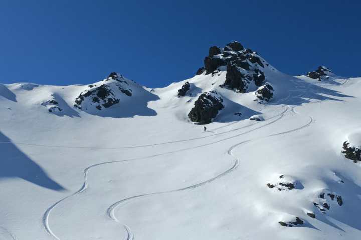 Snowy mountain slope with ski tracks and a clear blue sky.