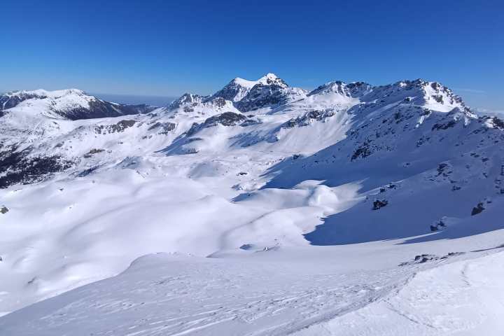Snow-covered mountains under a clear blue sky with rugged peaks and open snowfields.