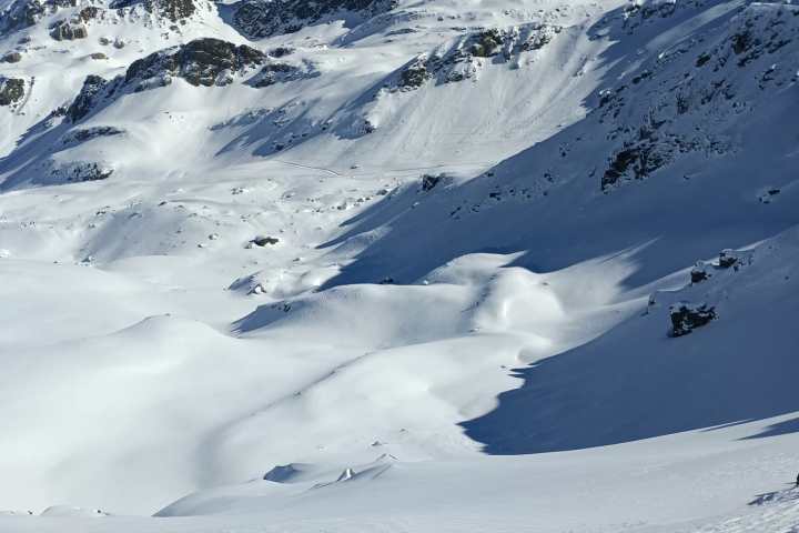 Snow-covered mountains under a clear blue sky, with sunlit slopes and rugged peaks.