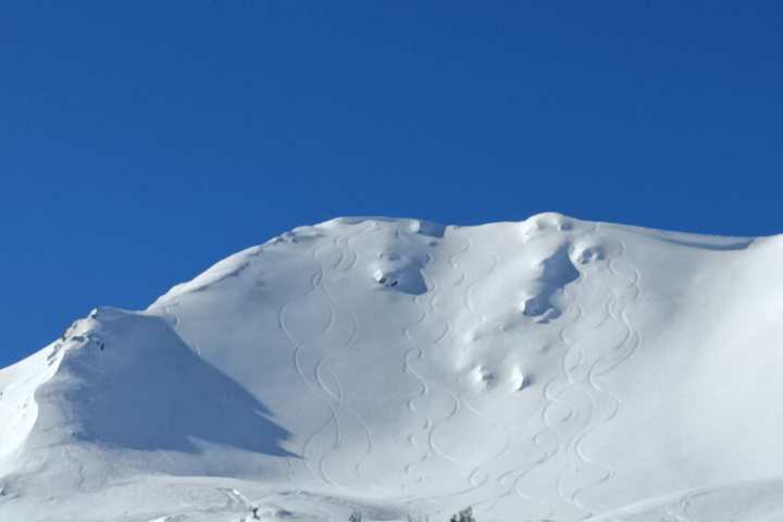 Snowy mountain peak with ski trails under a clear blue sky.
