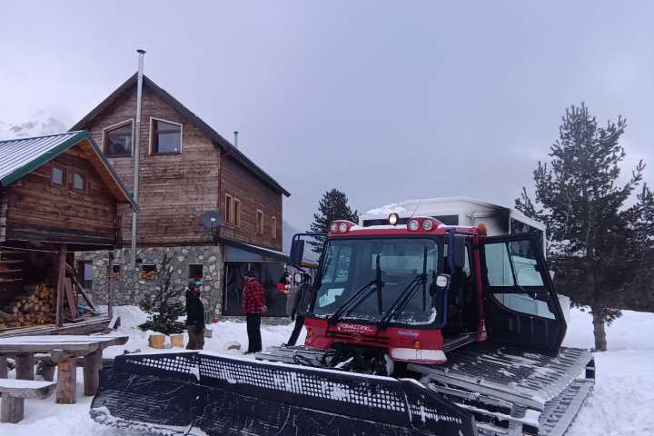 Snowcat vehicle parked in snowy area near a wooden cabin.