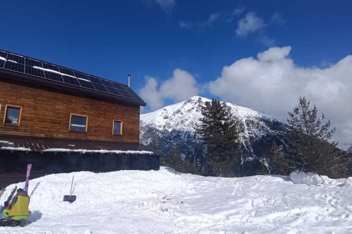 Snowy landscape with a wooden building, solar panels, and a mountain peak in the background.