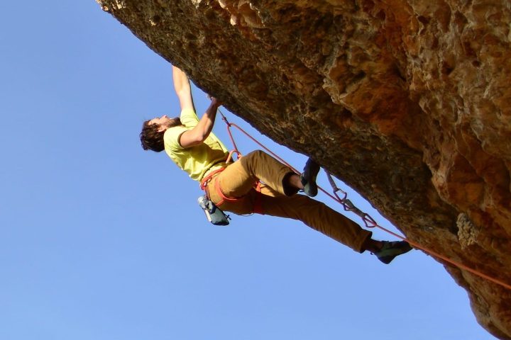 Person rock climbing on overhanging cliff with blue sky background.