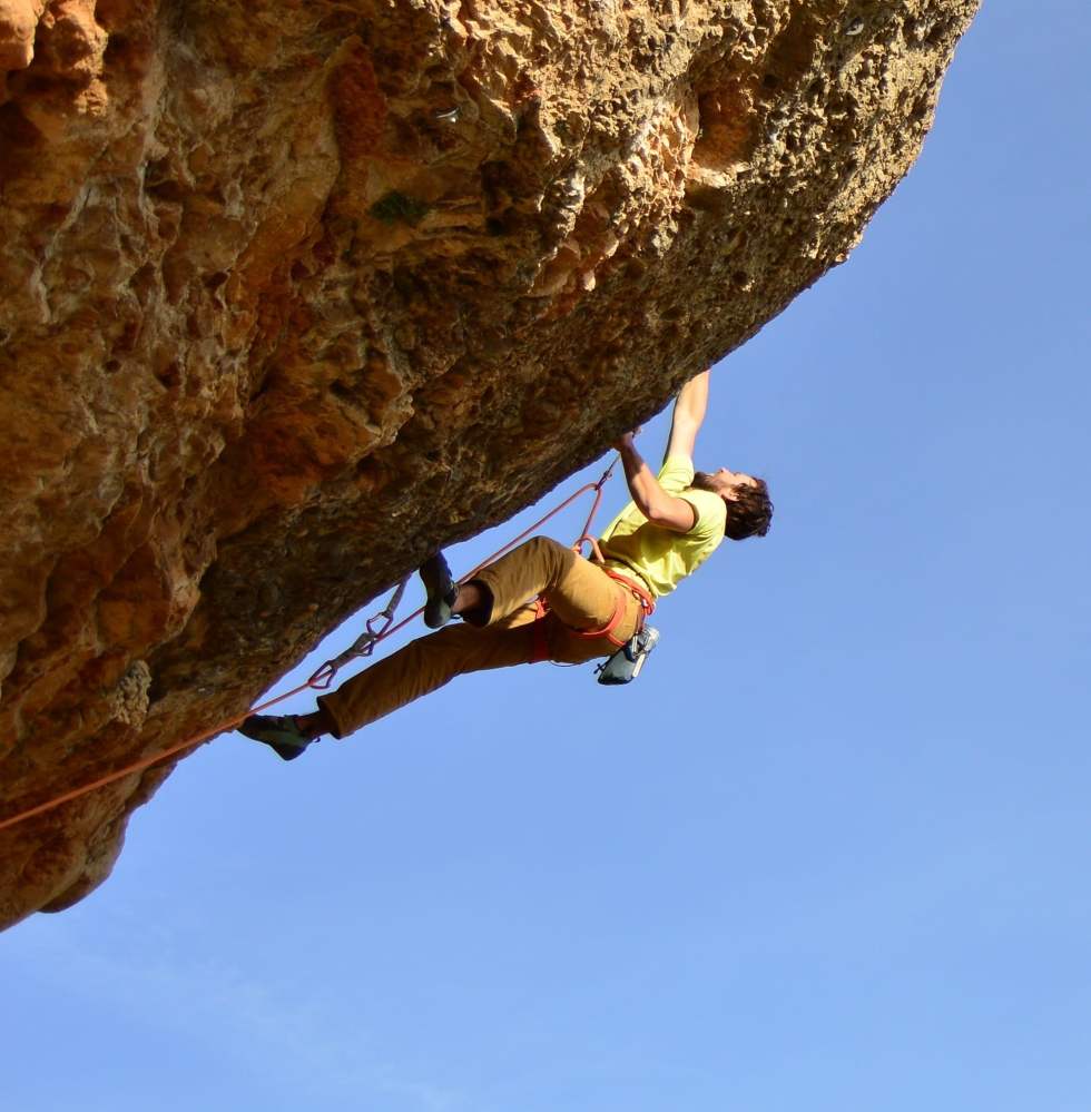 Person rock climbing on overhanging cliff with blue sky background.