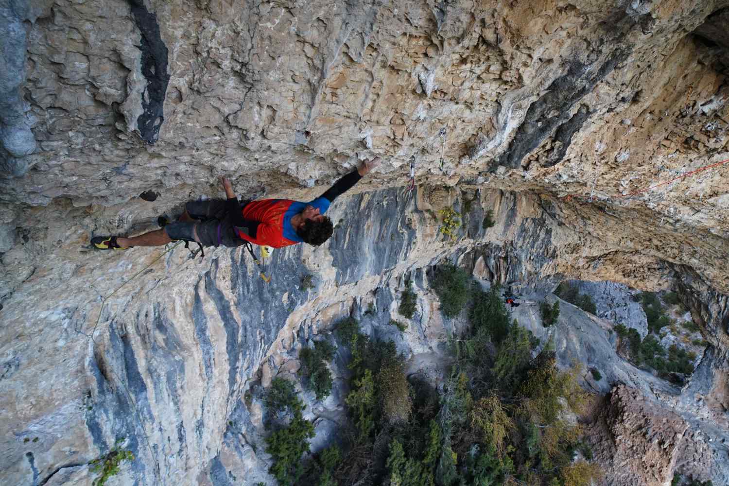 A climber in a red shirt ascends a steep rocky cliff face.