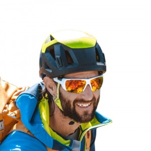 Smiling man with beard in helmet and sunglasses wearing outdoor gear.