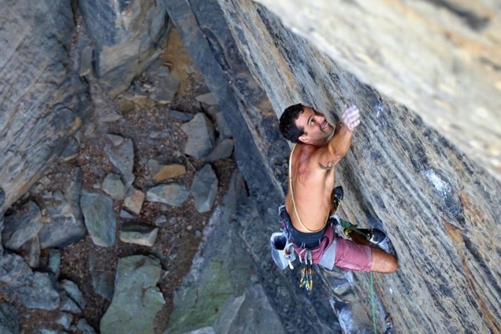 Person rock climbing on a vertical cliff face, equipped with climbing gear.