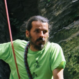 Man in bright green shirt rock climbing with a rope outdoors.