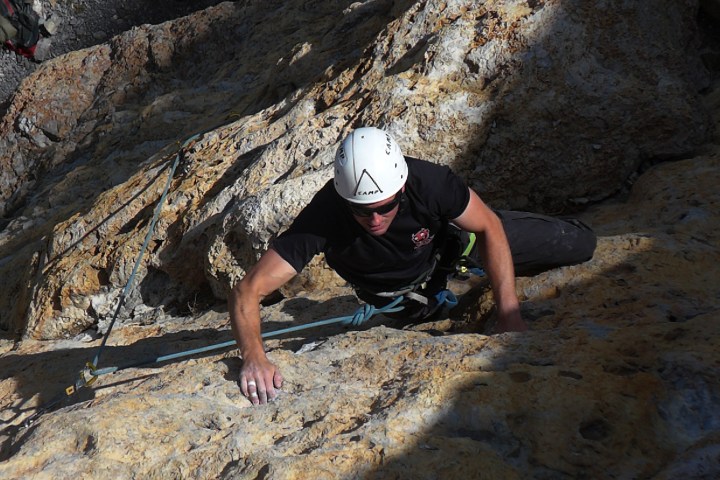 Rock climber in helmet ascending a steep, rocky surface.