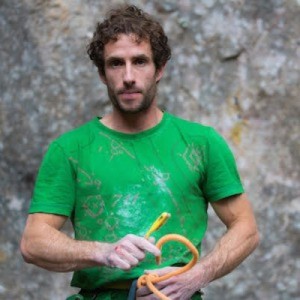 Man in green shirt holding climbing rope against a rock wall background.