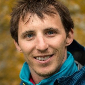 Smiling man in a blue jacket with a blurred autumn background.