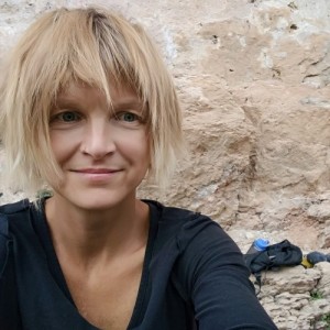 Person with short hair smiling in front of a rocky background.