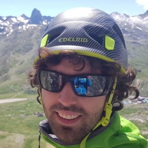 Person with helmet and sunglasses standing in a mountainous landscape.